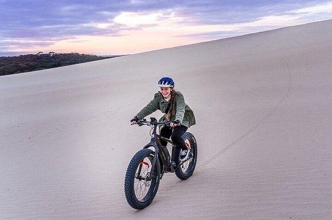 A fat bike riding across a white sand dune under a pink dusk sky