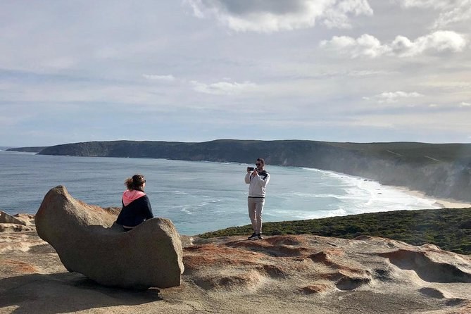 Two visitors on a granite dome above a long curved bay